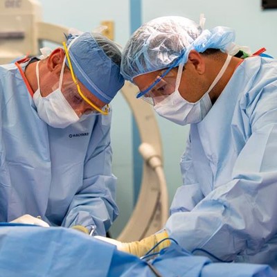 Two surgeons in blue scrubs and surgical masks performing a surgery in an operating room.