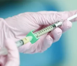 A person wearing a glove holding an injection